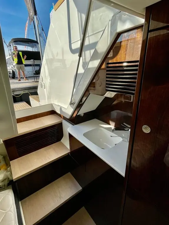 Interior view of a yacht's stairway, featuring wooden steps and a small sink area, with a person visible outside.